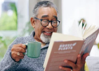 Homem idoso sorridente lê um livro enquanto toma seu café. Recomendando livros curtos para ler em um dia.