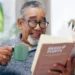 Homem idoso sorridente lê um livro enquanto toma seu café. Recomendando livros curtos para ler em um dia.