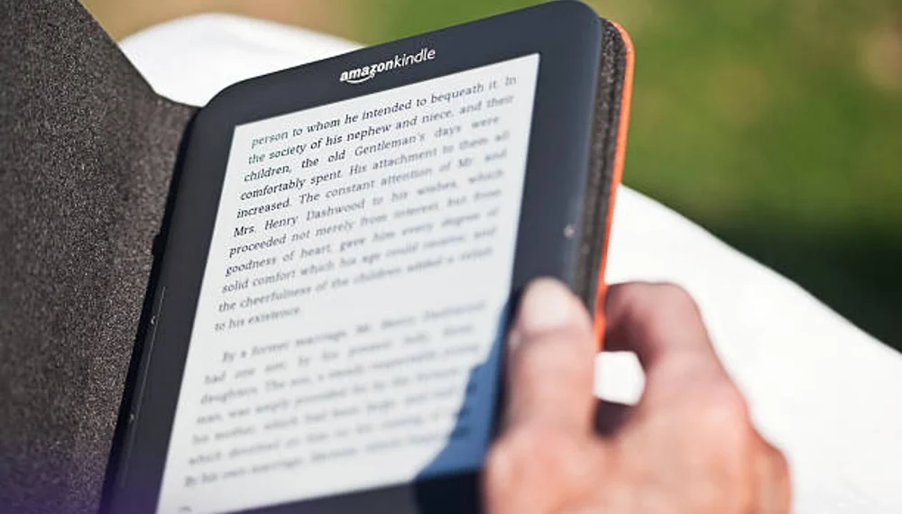 Pessoa manuseia o seu Amazon Kindle, que está protegido por uma capa preta. Falando sobre os melhores livros do Kindle Unlimited.