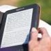 Pessoa manuseia o seu Amazon Kindle, que está protegido por uma capa preta. Falando sobre os melhores livros do Kindle Unlimited.